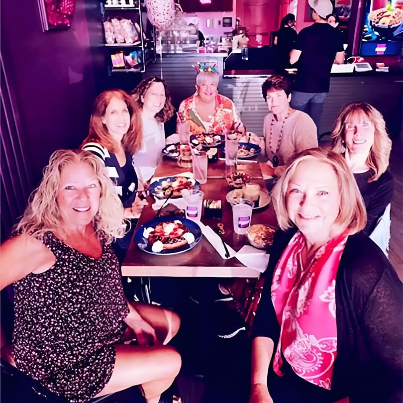 Seven smiling women enjoying a festive meal together at a restaurant table.