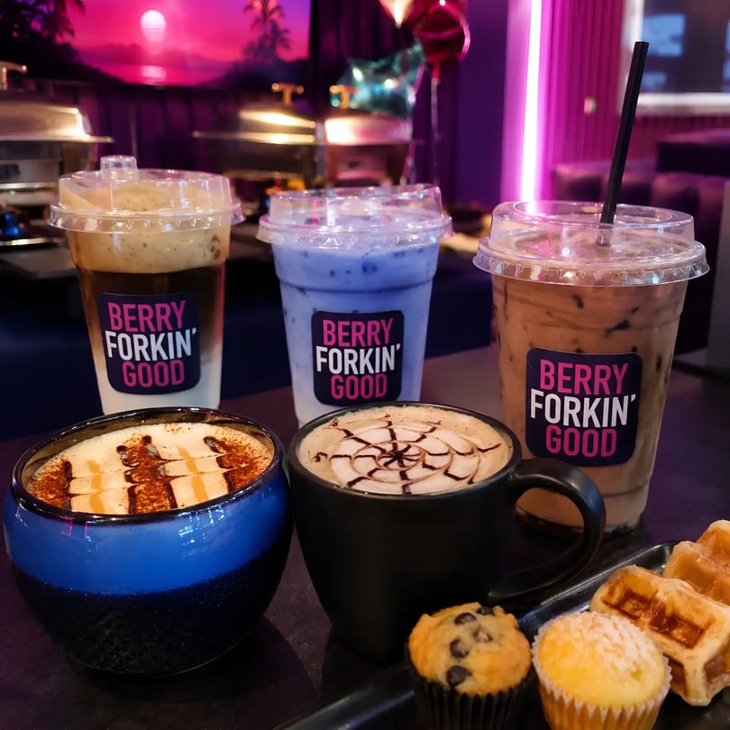 Assortment of hot and cold drinks with muffins and waffles on a table in a vibrant restaurant setting.