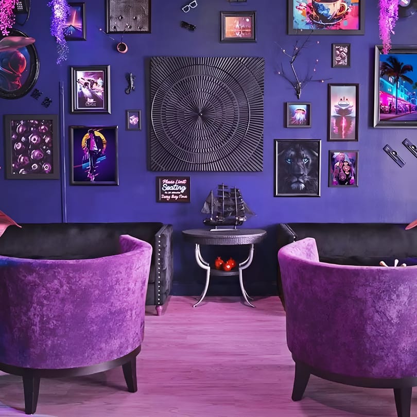 Eclectic purple lounge area featuring velvet chairs, black sofas, and a wall filled with diverse artwork.