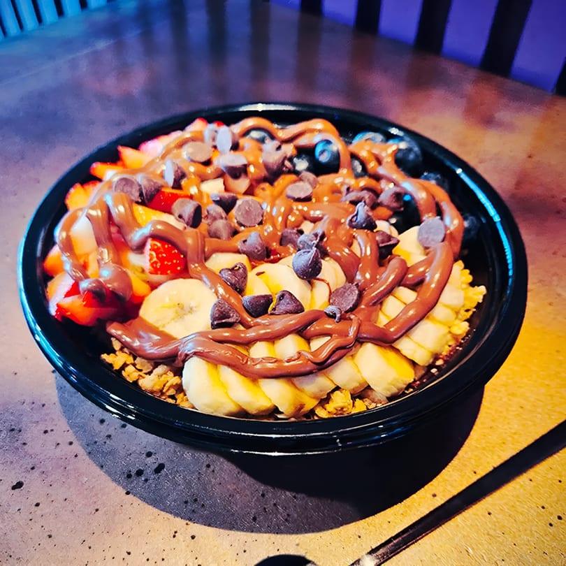 Vibrant fruit bowl with strawberries, bananas, blueberries, granola, chocolate drizzle, and chocolate chips.